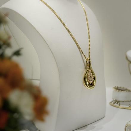 Pendentif doré en forme de goutte sur un buste de présentation blanc