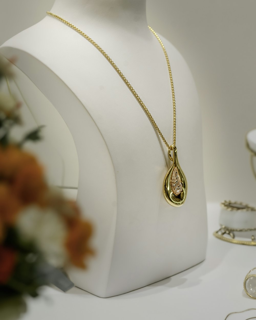 Pendentif doré en forme de goutte sur un buste de présentation blanc