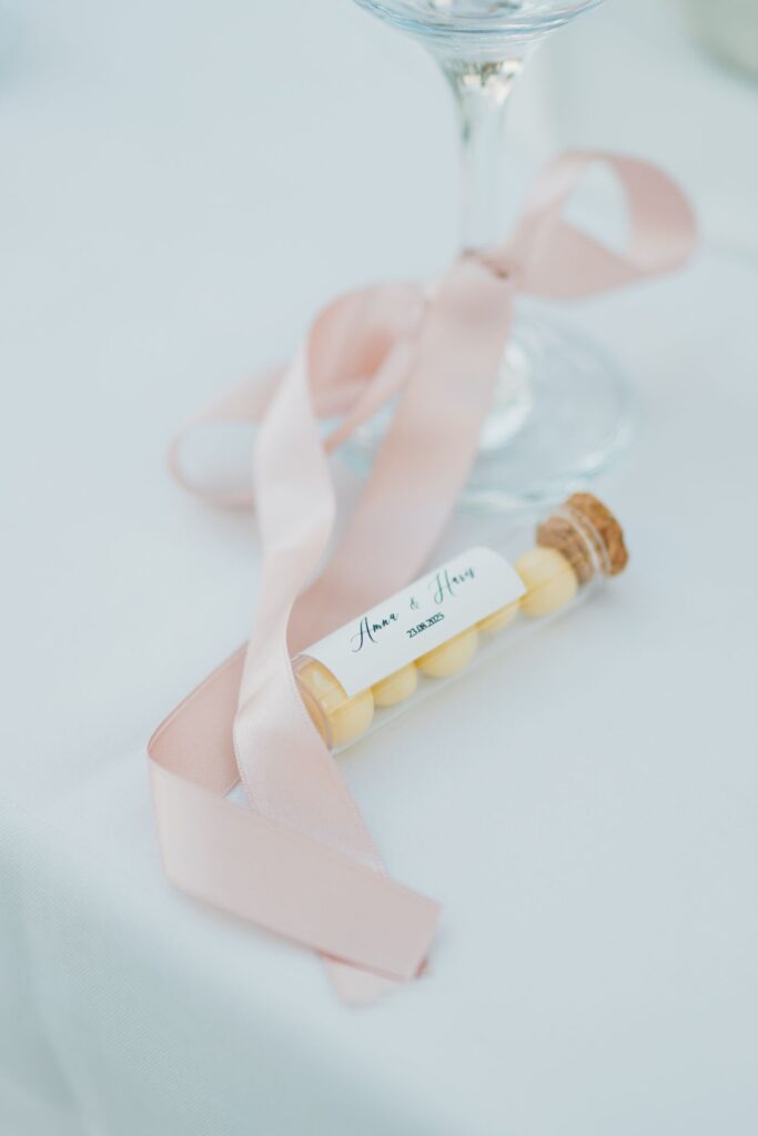 Tube de dragées fermé par un bouchon en liège et un ruban rose, avec une étiquette personnalisée