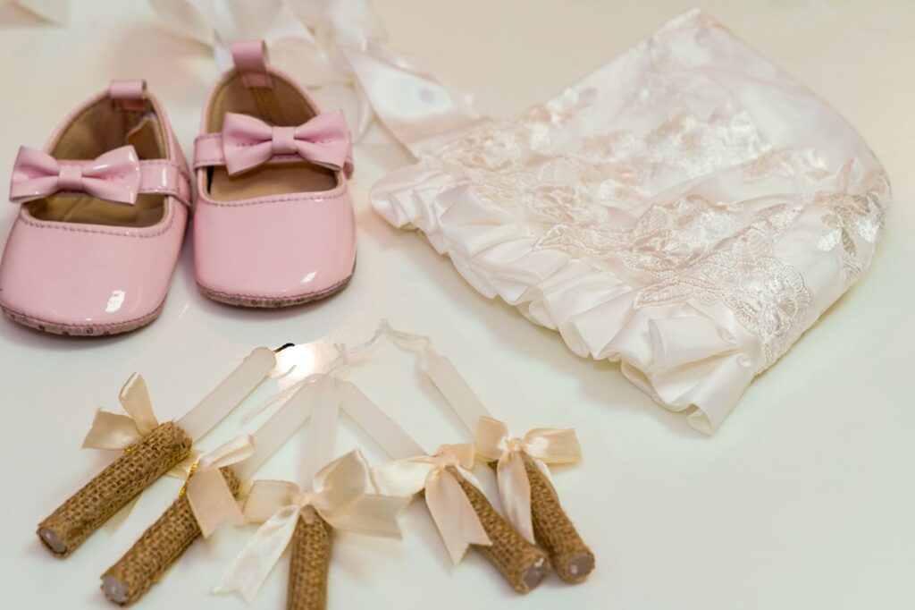 Chaussons roses, bonnet brodé et cierges ornés de rubans pour un baptême