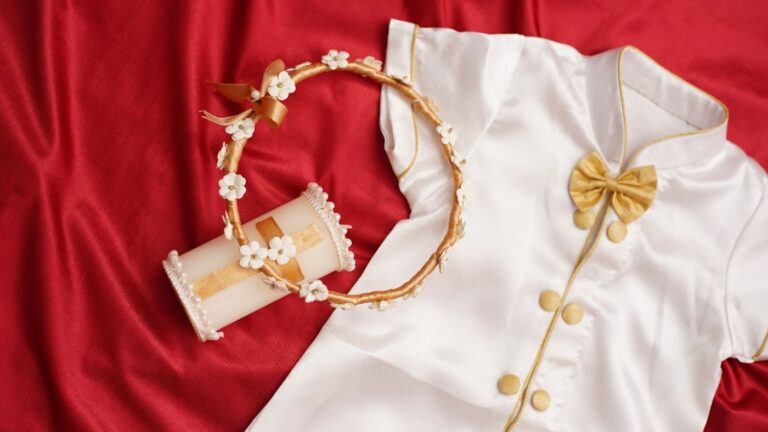 Tenue de baptême blanche, couronne de fleurs et cierge posés sur un tissu rouge
