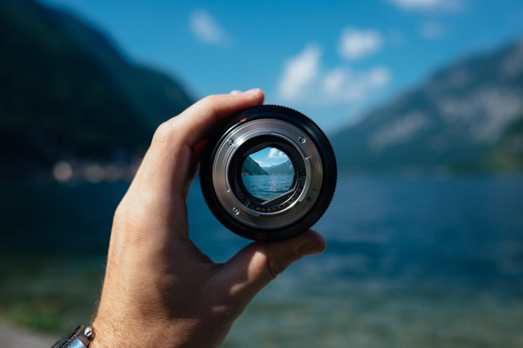 Objectif d'appareil photo tenu à la main cadrant un lac et des montagnes